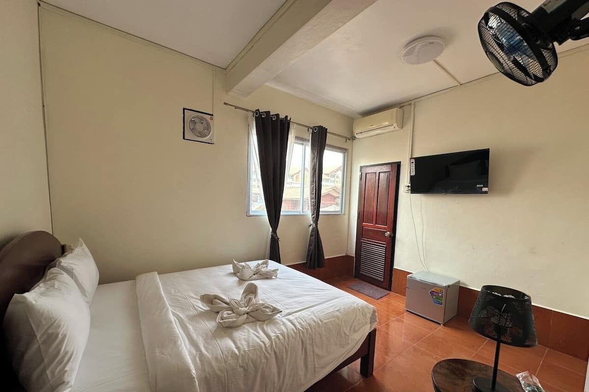 A hotel room with a bed, a TV, a fan, and a window with curtains.