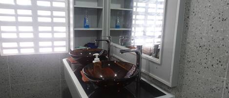 Un baño moderno con un lavabo de vidrio negro, encimera blanca y un espejo sobre el lavabo.