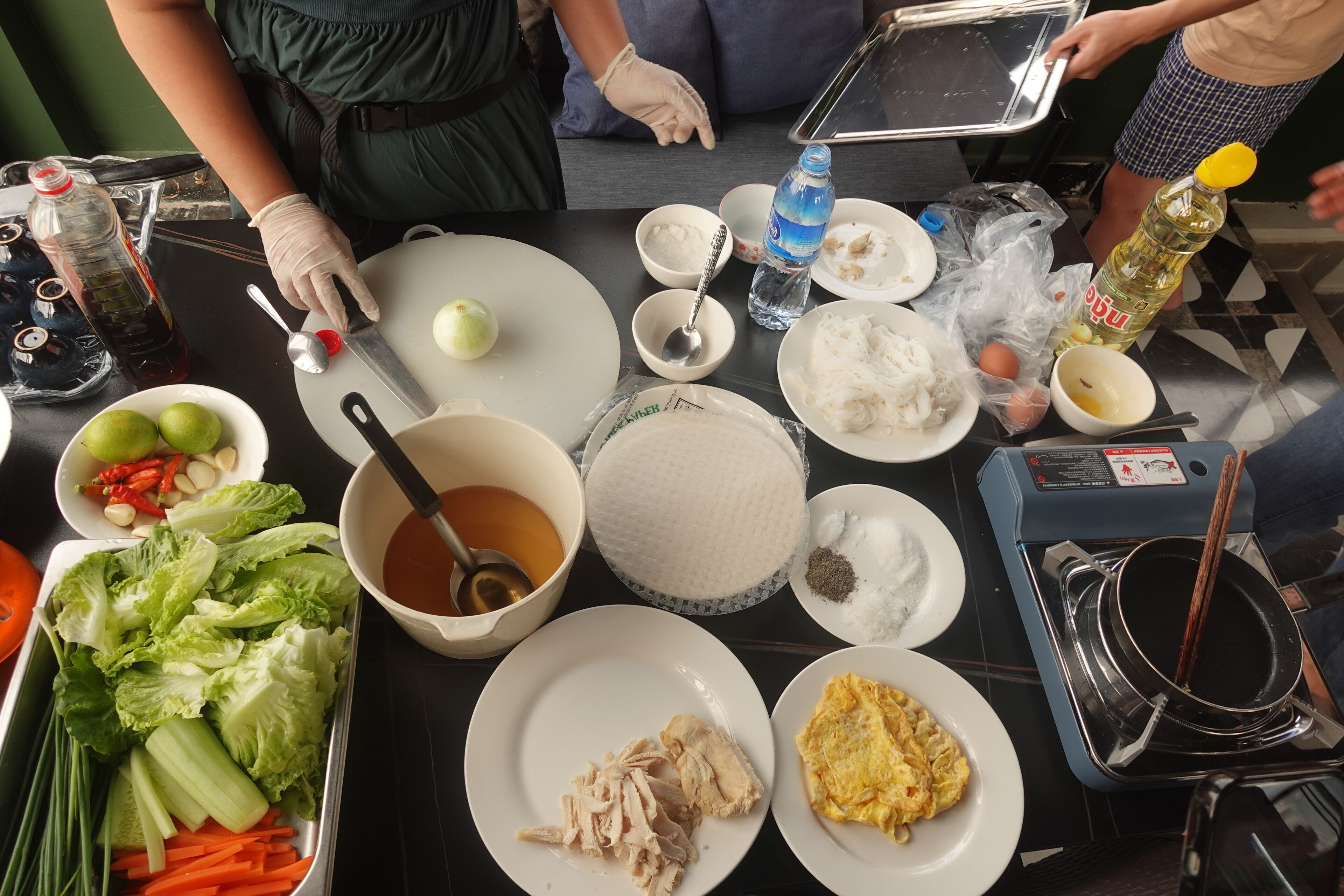 Uma mesa com diversos alimentos e acompanhamentos, incluindo arroz, vegetais e uma tigela de sopa.