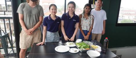 A group of people standing at a table with plates, bowls, and a tray of food.
