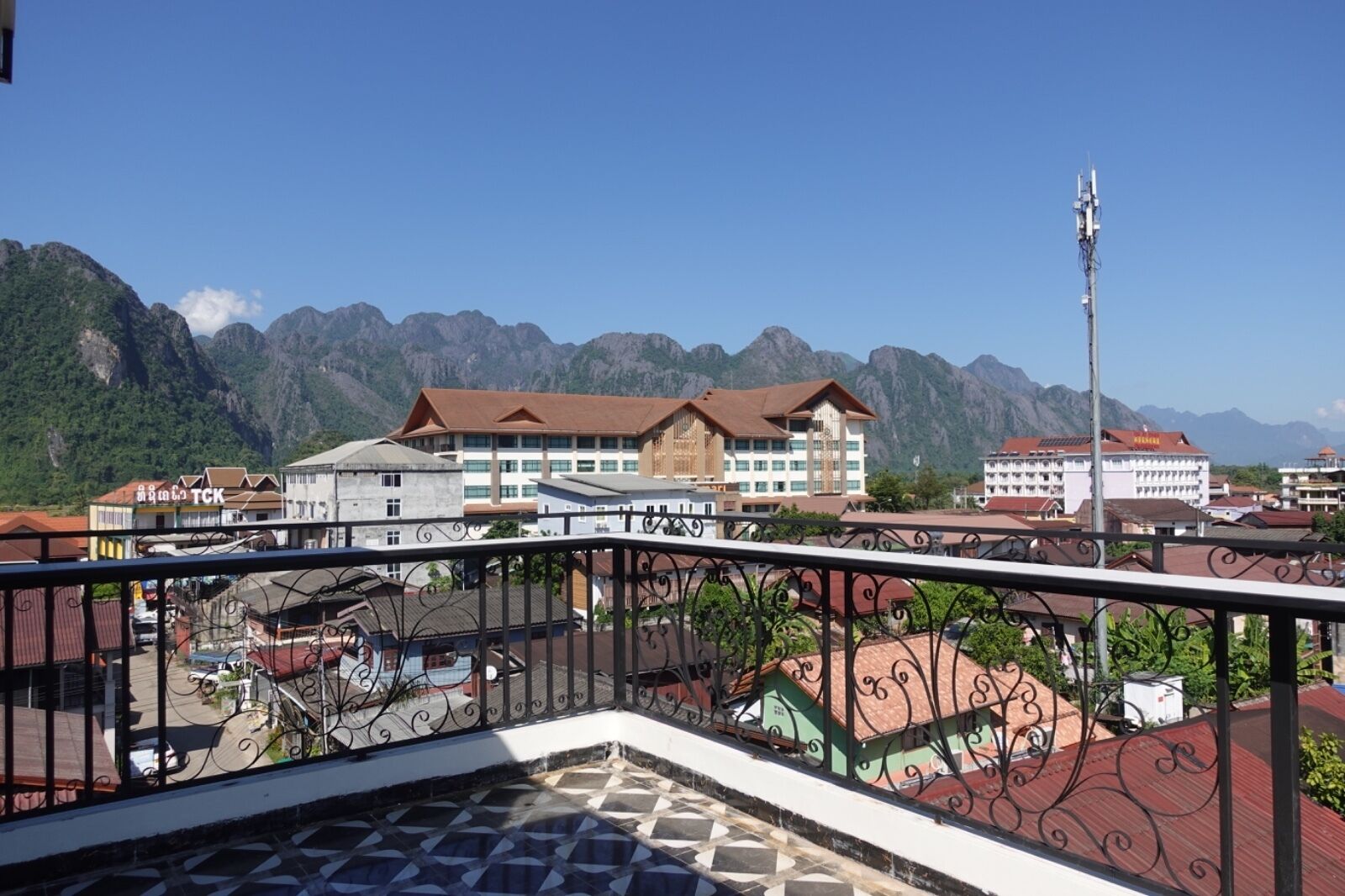 Un hotel con montañas al fondo, que cuenta con un balcón con piso estampado y barandilla de metal.