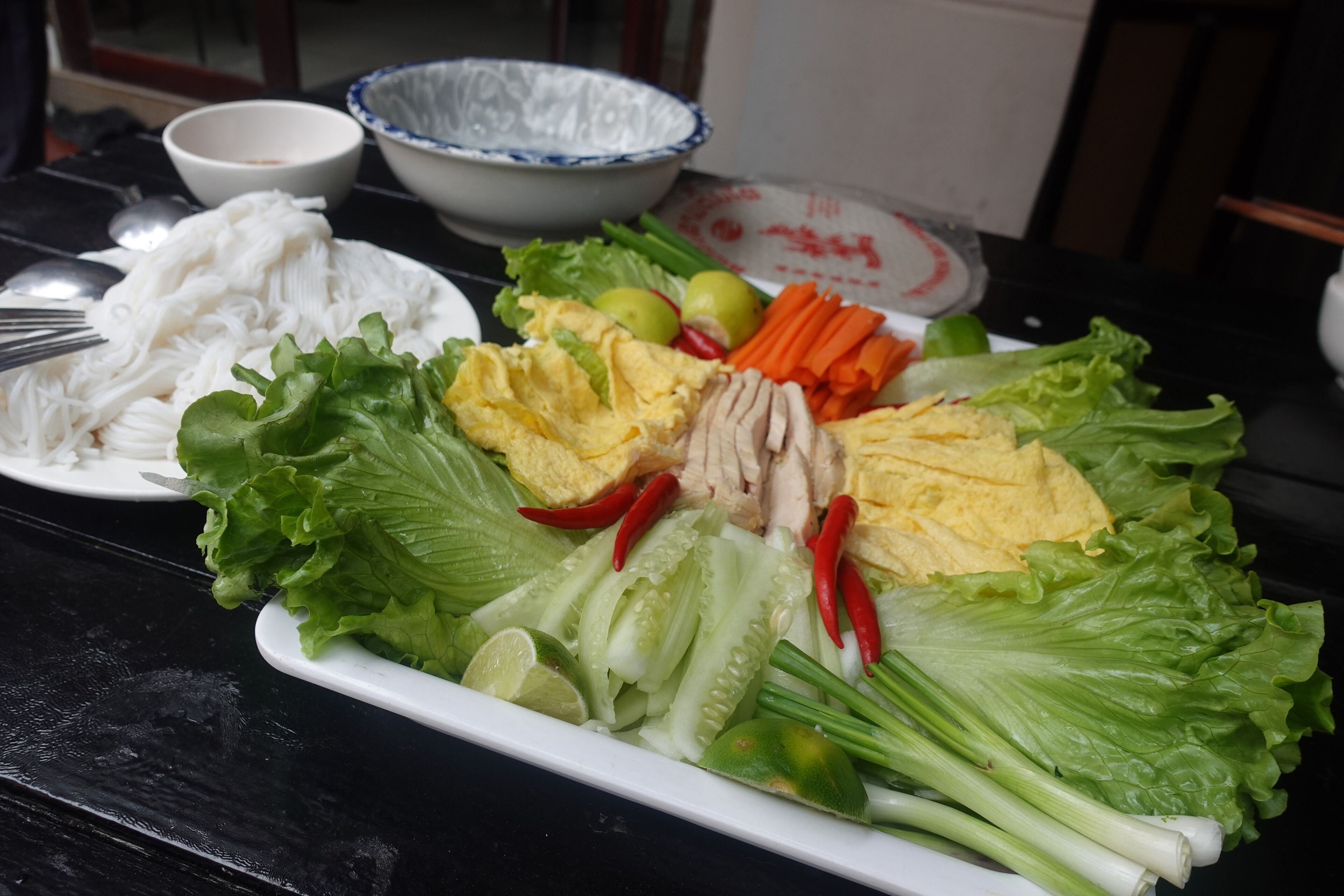 A table with a variety of fresh vegetables and a plate of noodles.