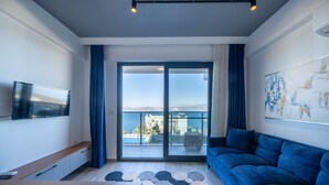 Una sala moderna con un sofá azul, un televisor de pantalla plana, una mesa de centro y un ventanal con vistas a la ciudad.
