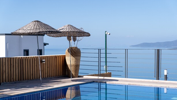Una piscina con dos sombrillas de paja, una valla de madera y vista al mar.