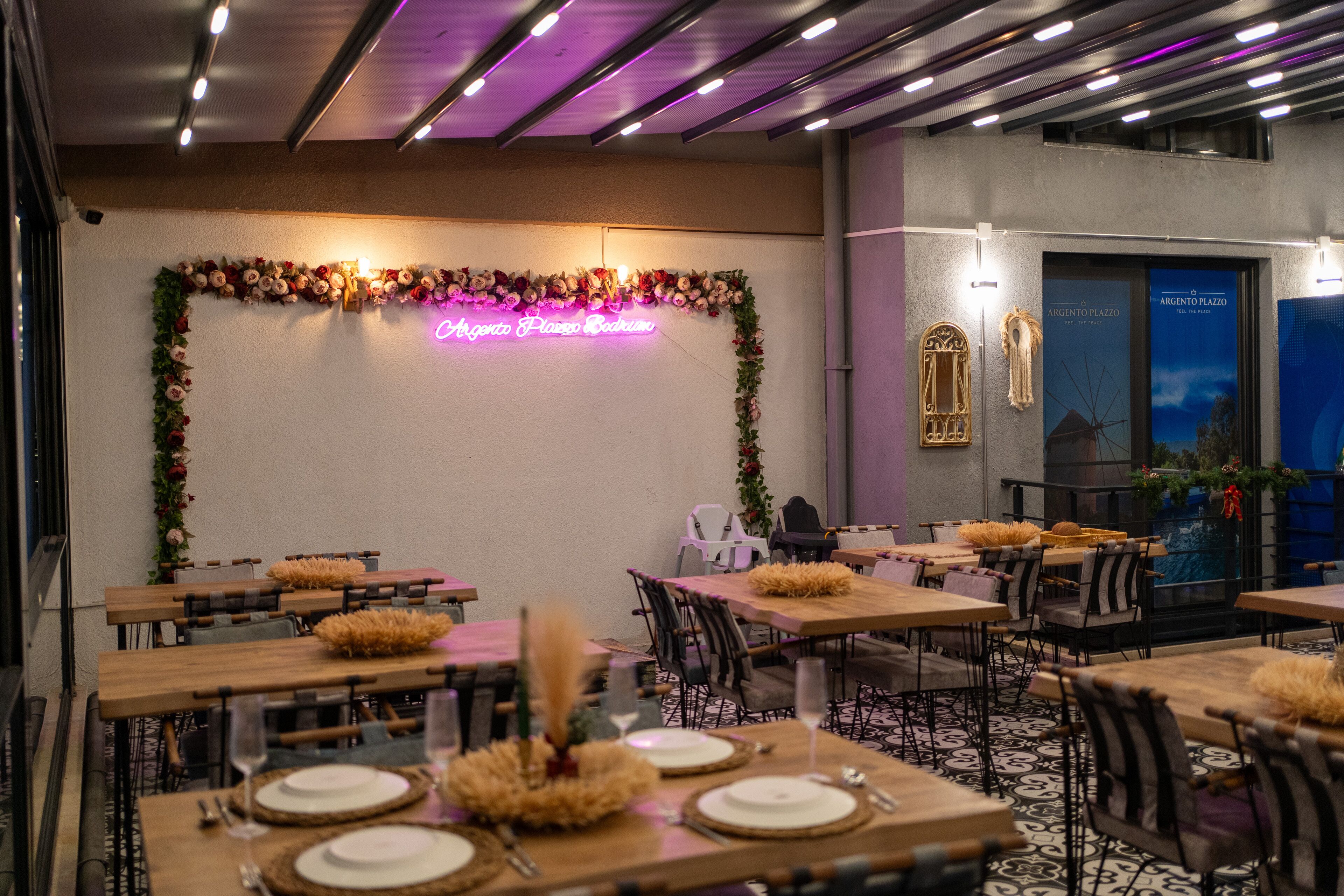 A restaurant with wooden tables and chairs, a neon sign, and a decorative wall.
