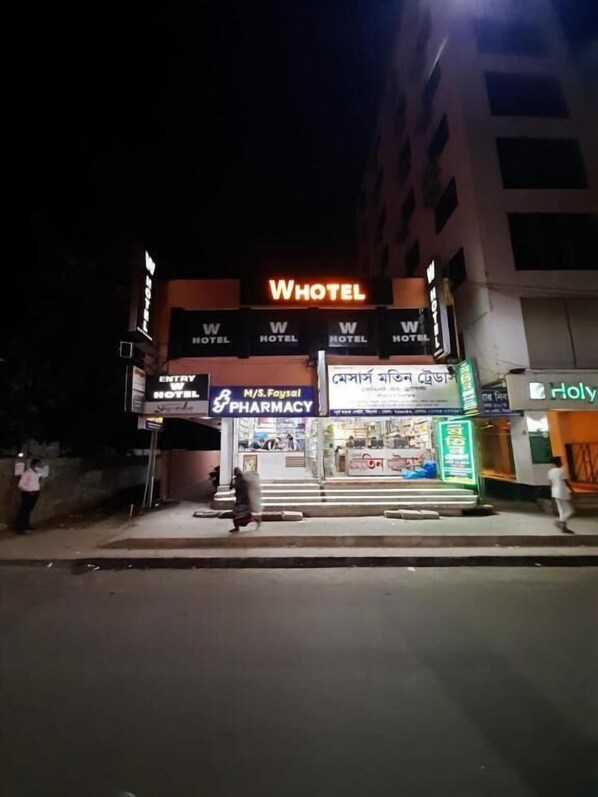 Un edificio con varios letreros de WHOTEL, una farmacia y una entrada visible.