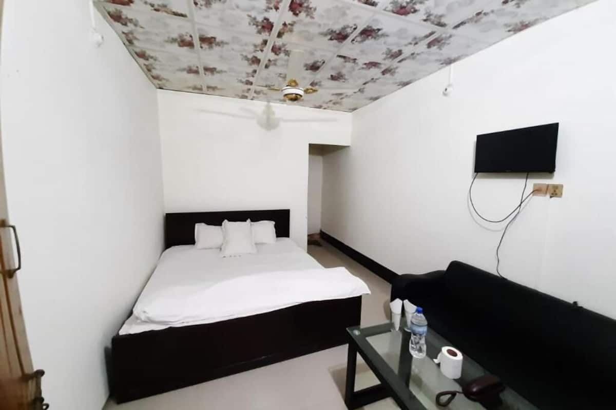 Un dormitorio con cama, televisor, mesita de vidrio con artículos de aseo y techo con motivos florales.