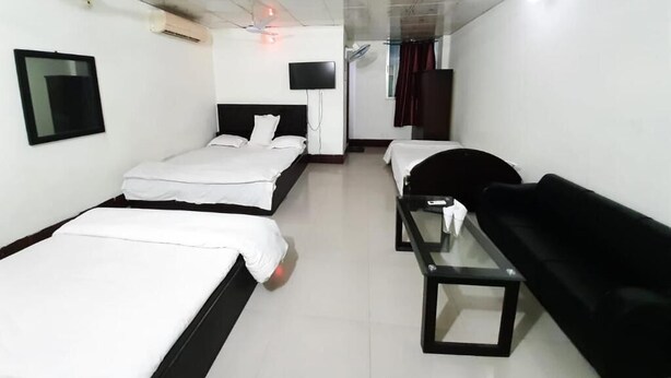 A hotel room with two beds, a black sofa, a small table, a TV, and a ceiling fan.