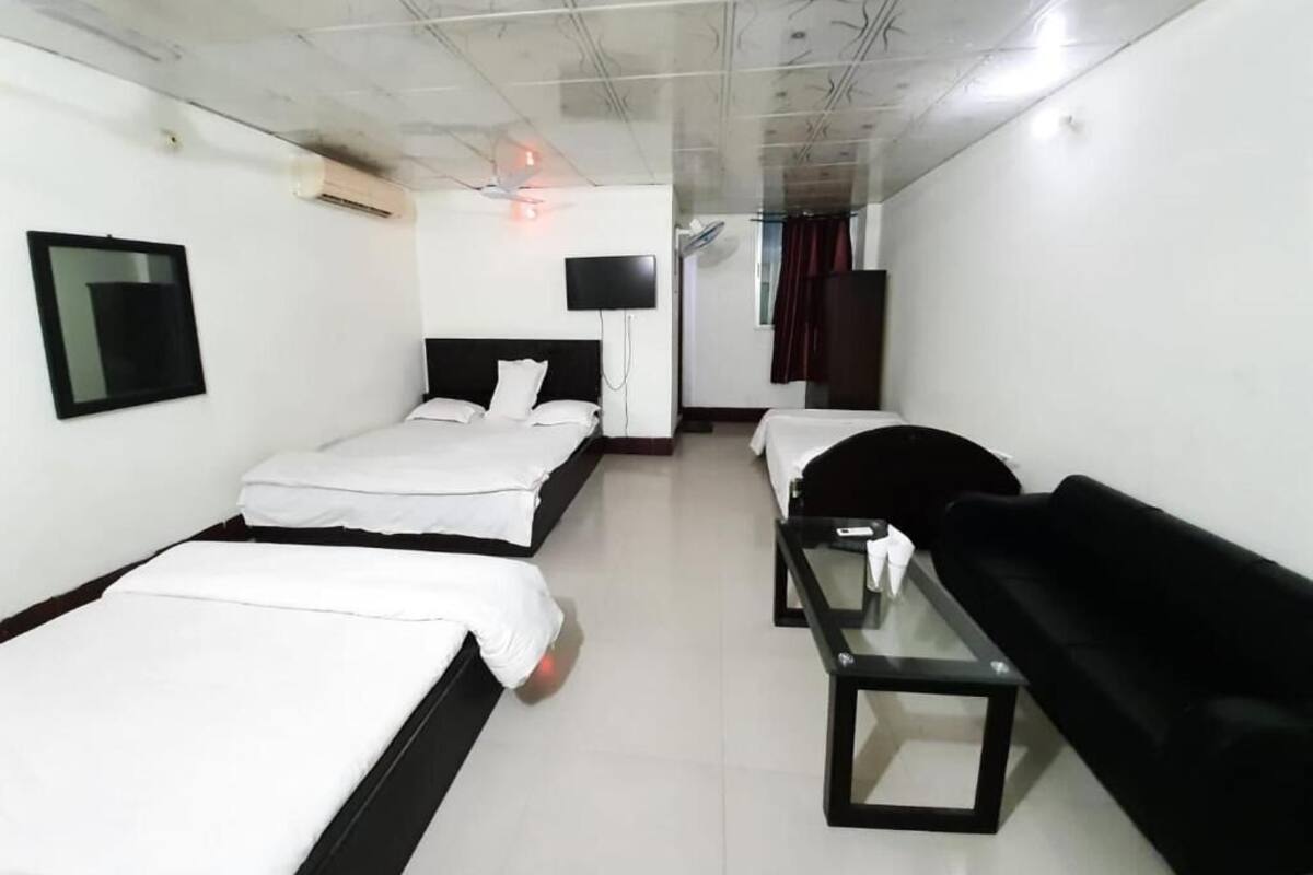 Una habitación de hotel con dos camas, un sofá negro, una mesita, un televisor y un ventilador de techo.