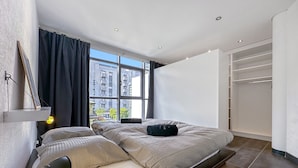 A modern bedroom with a large window, a bed with a headboard, a bedside table with a lamp, and a walk-in closet. - Dolce Vita in the Swiss Alps - Close to 4 Valleys (Martigny)