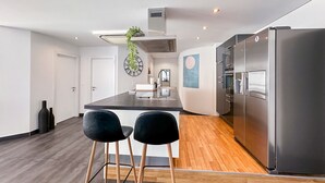 A modern kitchen with a central island, two black bar stools, a stainless steel refrigerator, and a wooden floor. - Dolce Vita in the Swiss Alps - Close to 4 Valleys (Martigny)