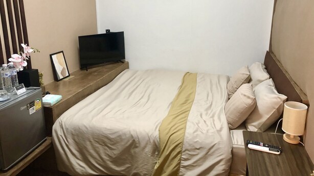 Une chambre d’hôtel avec un lit, une télévision, une table de chevet avec une lampe et un petit bureau avec une bouteille d’eau et un cadre photo.