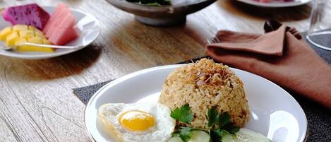 A plate of fried rice with an egg, cucumber slices, and tomato, accompanied by a bowl of dessert and a plate of fruit.