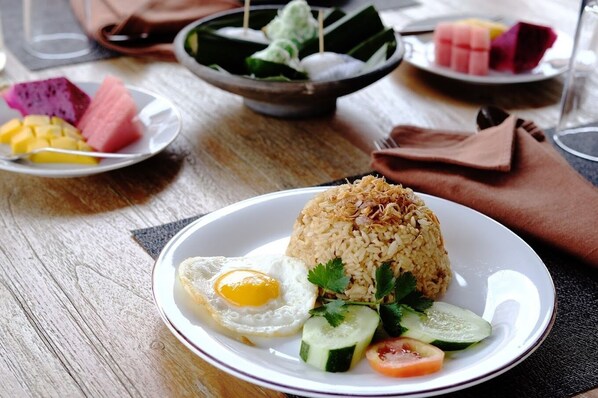 A plate of fried rice with an egg, cucumber slices, and tomato, accompanied by a bowl of dessert and a plate of fruit. - Bhumi Kasuryan (Borobudur)