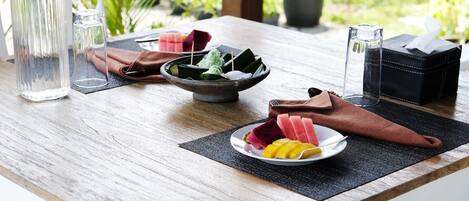 A wooden table with a plate of fruit, a glass of water, a bowl of food, and a napkin.
