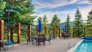 An outdoor pool area with a metal fence, seating, and umbrellas. - Free Ski Locker@Resort Base-Views-Pool-HotTub-Grill-Deck+Walk to Mtn/Trails/Eat/Drink/Free Town Bus (Steamboat Springs)
