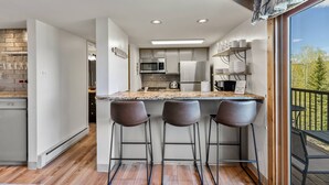 A modern kitchen with a central island, bar stools, and a view of the outdoors. - Free Ski Locker@Resort Base-Views-Pool-HotTub-Grill-Deck+Walk to Mtn/Trails/Eat/Drink/Free Town Bus (Steamboat Springs)