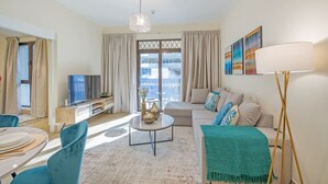A modern living room with a sofa, a coffee table, and a TV. There is a balcony with curtains and a view of the city. - Stylish 2BR with Balcony Near Dubai Mall & Burj Khalifa (Oldtown Dubai)