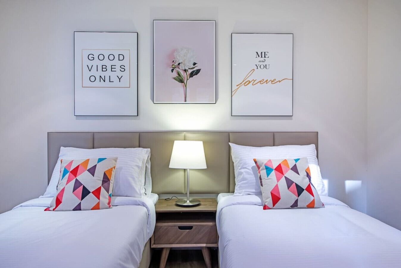 Ein Hotelzimmer mit zwei Betten, einem Nachttisch mit Lampe und drei gerahmten Bildern an der Wand.