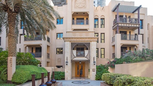 A multi-story building with a central entrance, balconies, and surrounding greenery. - Stylish 2BR with Balcony Near Dubai Mall & Burj Khalifa (Oldtown Dubai)