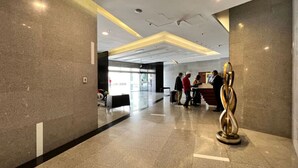 Een moderne lobby met een receptiebalie, een zithoek en een decoratief beeldhouwwerk.