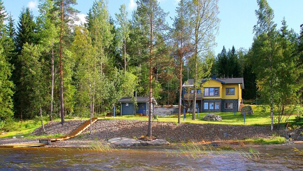 Un chalet doté d’un quai en pierre qui s’avance dans une rivière, entouré d’une forêt dense.