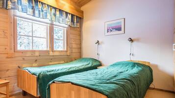 A room with two wooden beds, a window with curtains, a painting on the wall, and a lamp.