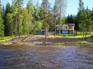 A lakeside cabin with a dock, surrounded by dense forest and a clear sky.