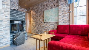 Une pièce chaleureuse avec un mur en pierre, une cheminée, un canapé rouge et une table en bois.