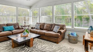 A sunroom with a brown leather sofa, a coffee table, and a ceiling fan. - Salty Shores (St. Augustine)