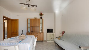 Um quarto com uma mesa de jantar posta para dois, um sofá, um aparador com portas de vidro e uma televisão sobre um suporte.