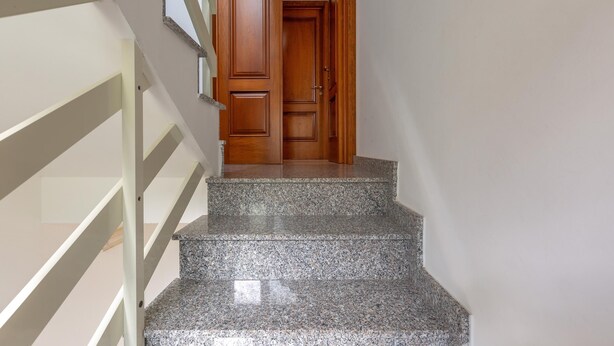 Uma escadaria com degraus de granito que leva a uma porta de madeira.