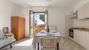 Uma cozinha compacta com uma mesa de jantar posta para dois, um guarda-roupa de madeira, e vista para o exterior por uma porta aberta.