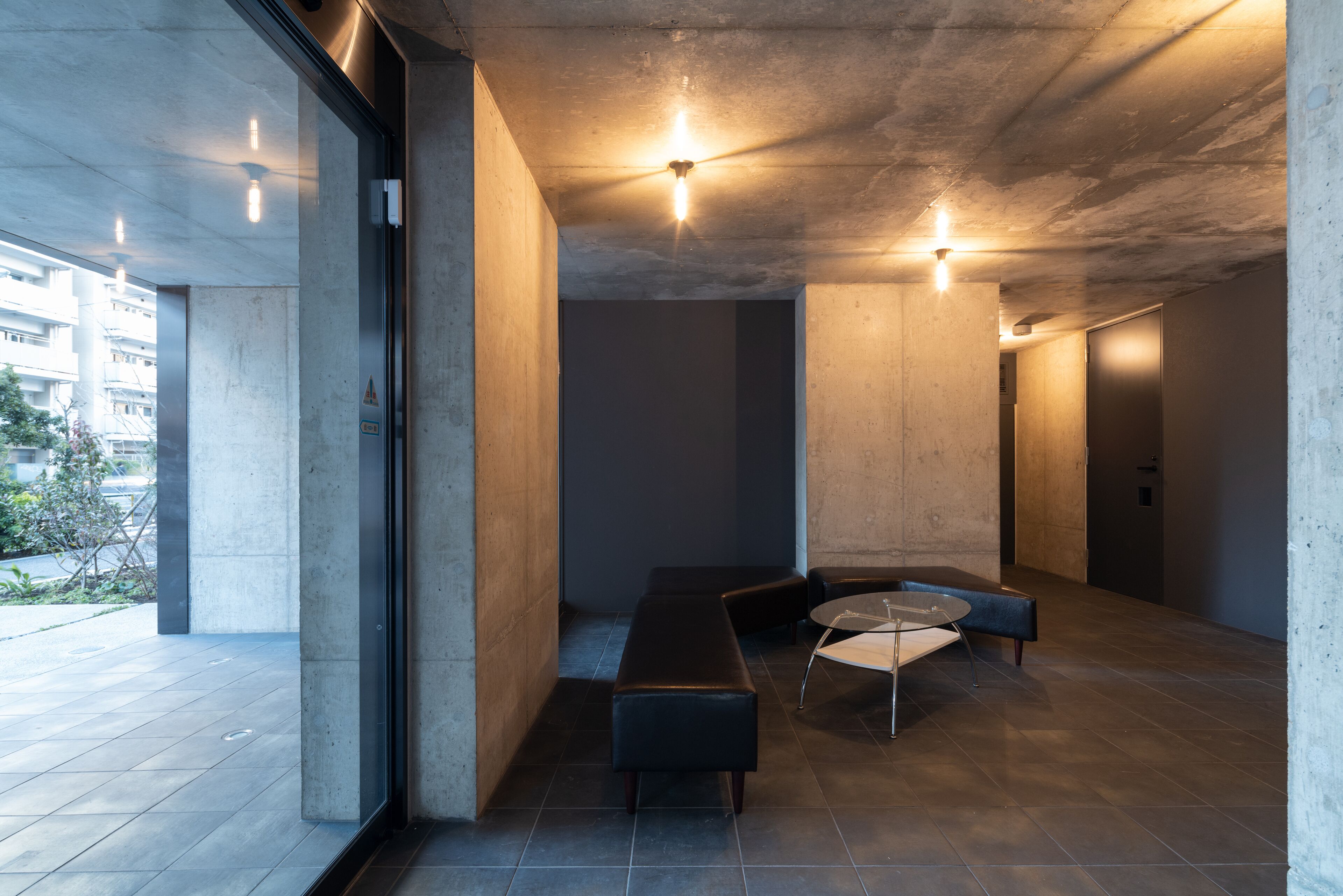 A modern interior with a concrete ceiling, a bench, a round table, and a glass wall.