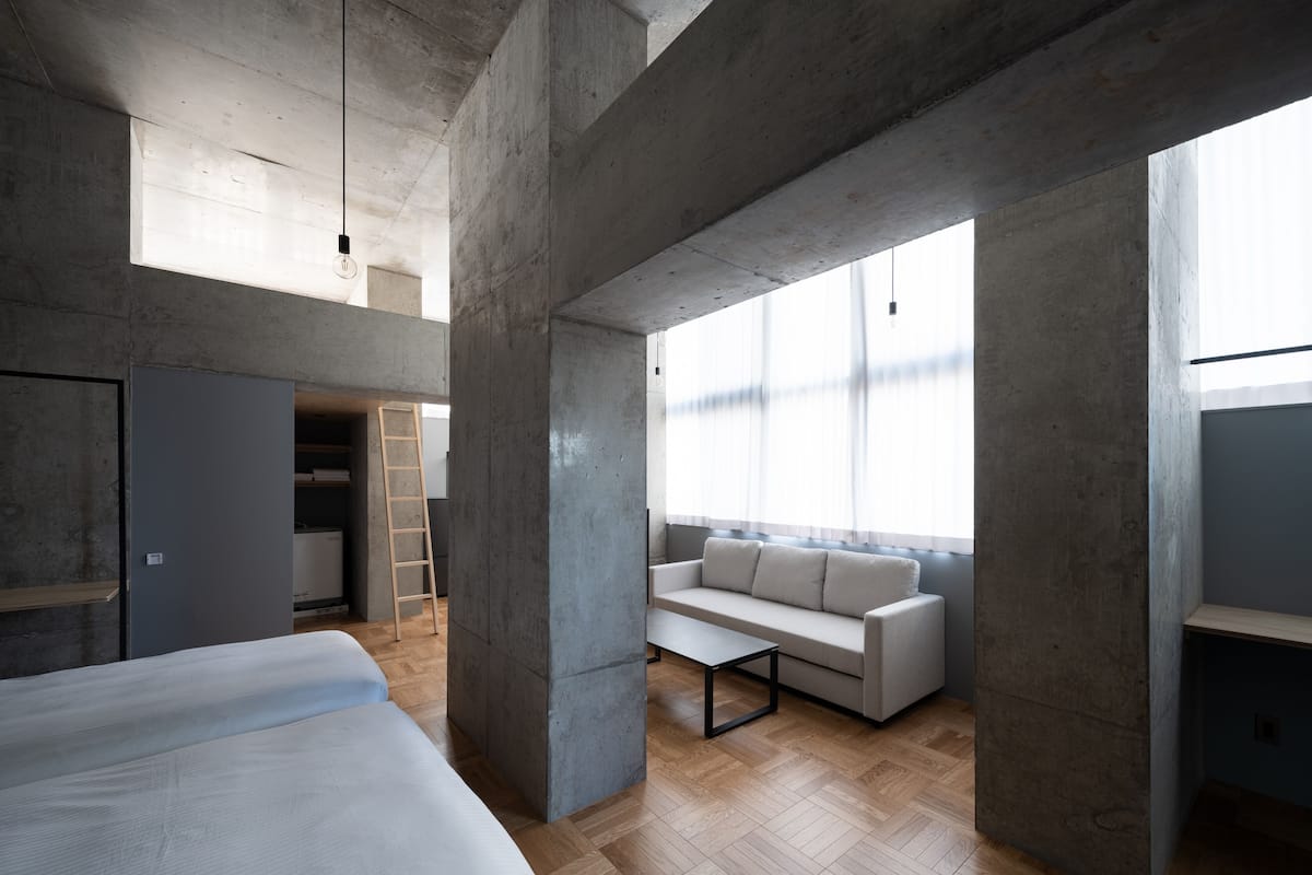 Um interior moderno com vigas de concreto aparente, um sofá, uma cama e um chão de madeira.