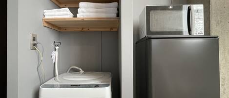 Una cocina compacta con lavadora integrada, microondas y repisa con toallas dobladas.