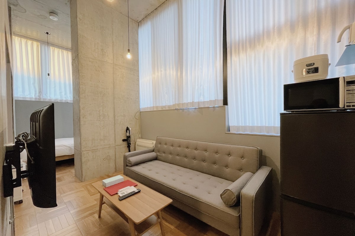 Um espaço compacto com sofá, uma mesa pequena, televisão e micro-ondas.