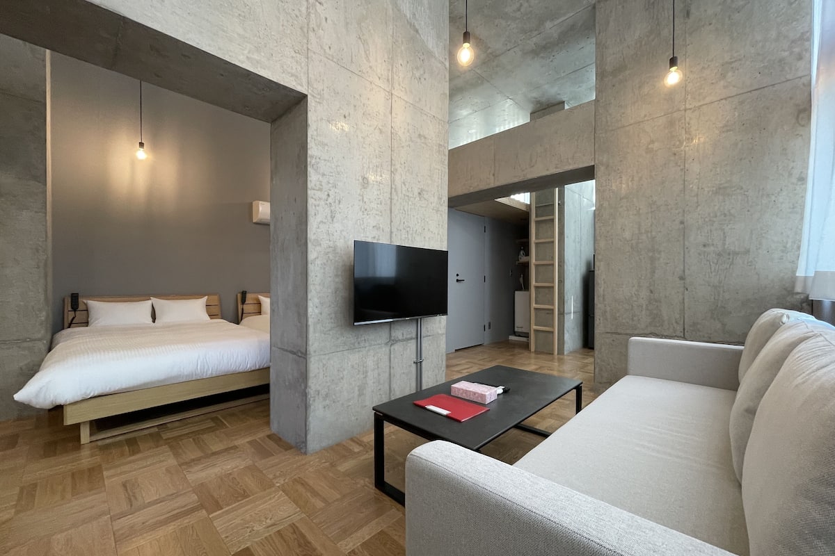 Quarto de hotel moderno com cama, sofá, televisão e mesa de centro.
