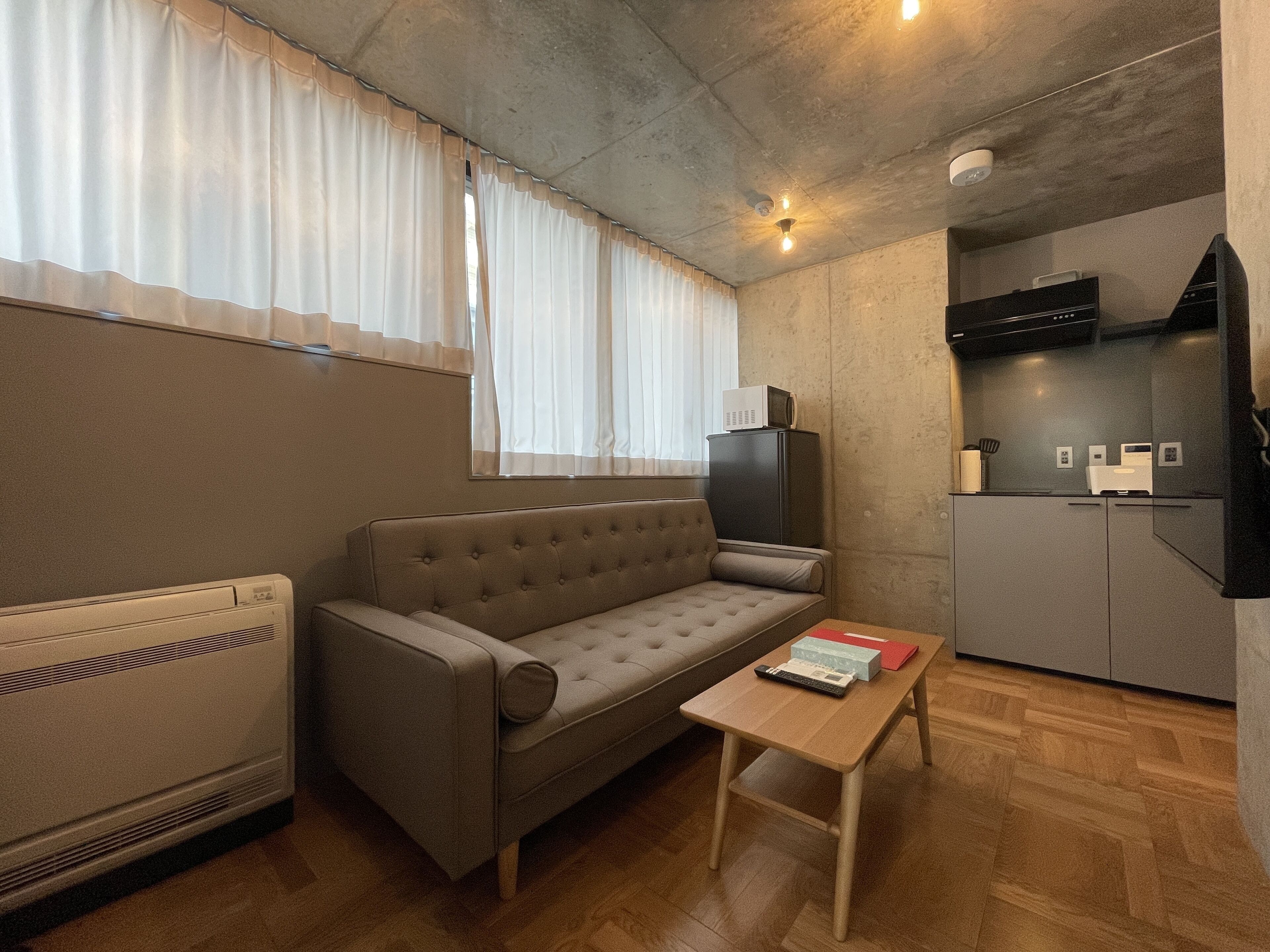 A compact living space with a sofa, a small table, a kitchenette, and a radiator.