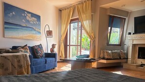 A spacious living room with a large bed, a blue sofa, a fireplace, and a view of greenery through the windows. - La Scalinatella in Mondello (Palermo)
