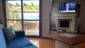 A living room with a blue sofa, a fireplace, and a TV displaying a news program. - La Scalinatella in Mondello (Palermo)