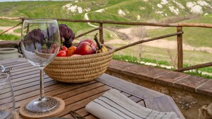 A table with a glass of wine, a woven basket of fruits, and a view of green hills.