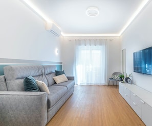 A modern living room with a grey sofa, a flat-screen TV mounted on the wall, and a wooden floor. - Silverius- Rome's Delightful Lodges {Vatican} Elegant 2 rooms 1 bath kitchen (Roma)