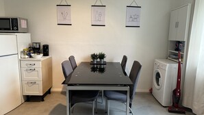 Una cucina compatta con un tavolo da pranzo, sedie, un forno a microonde, una macchina per il caffè e una lavatrice.