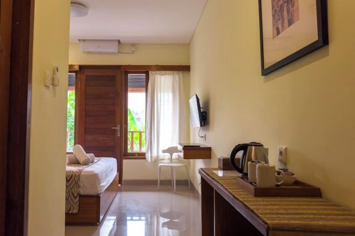 Una camera d'albergo con un letto, una scrivania con bollitore, una sedia e una TV appesa al muro.
