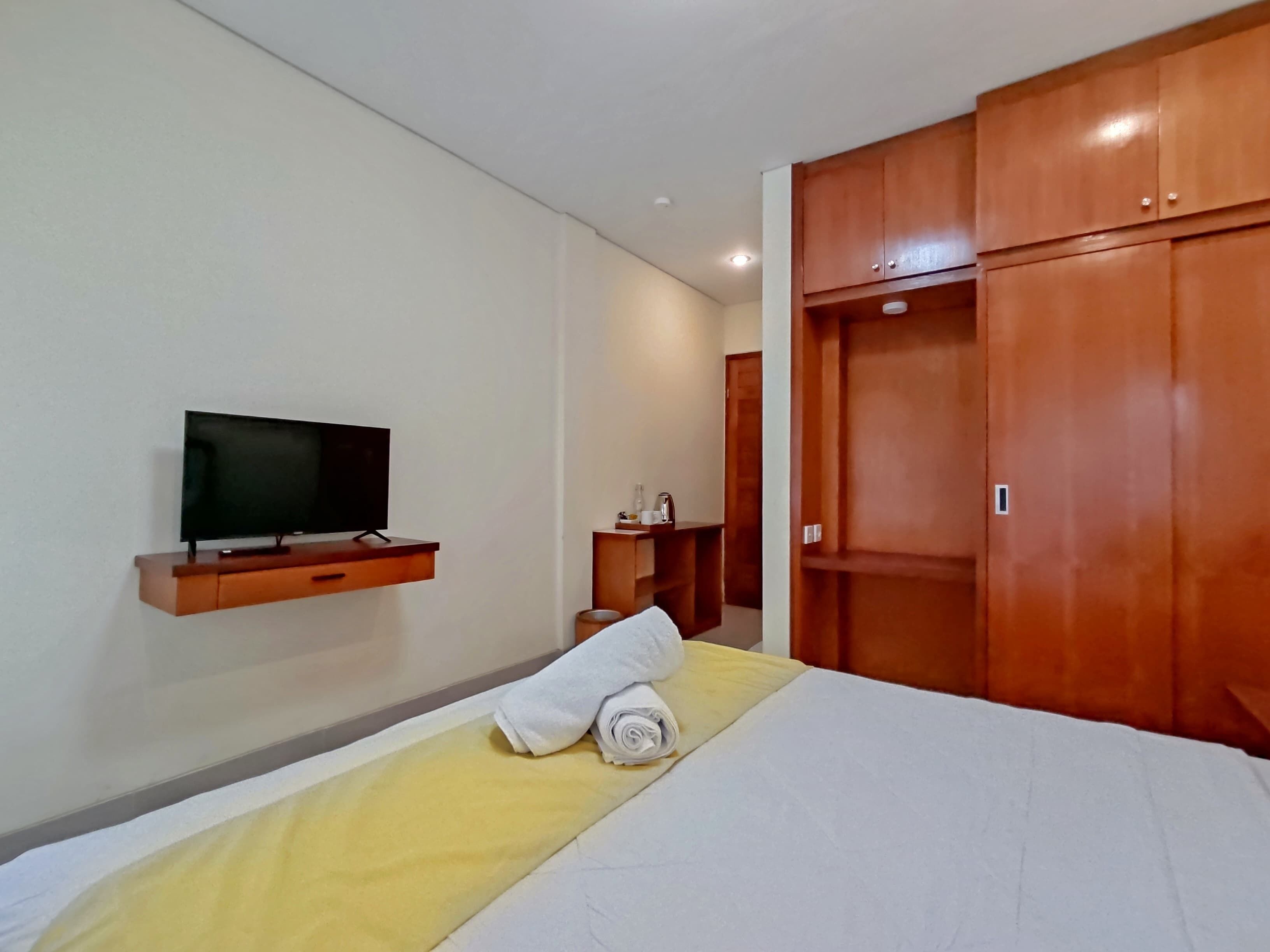 Une chambre d’hôtel avec un lit, un téléviseur fixé au mur, des armoires en bois et une petite table avec une lampe.