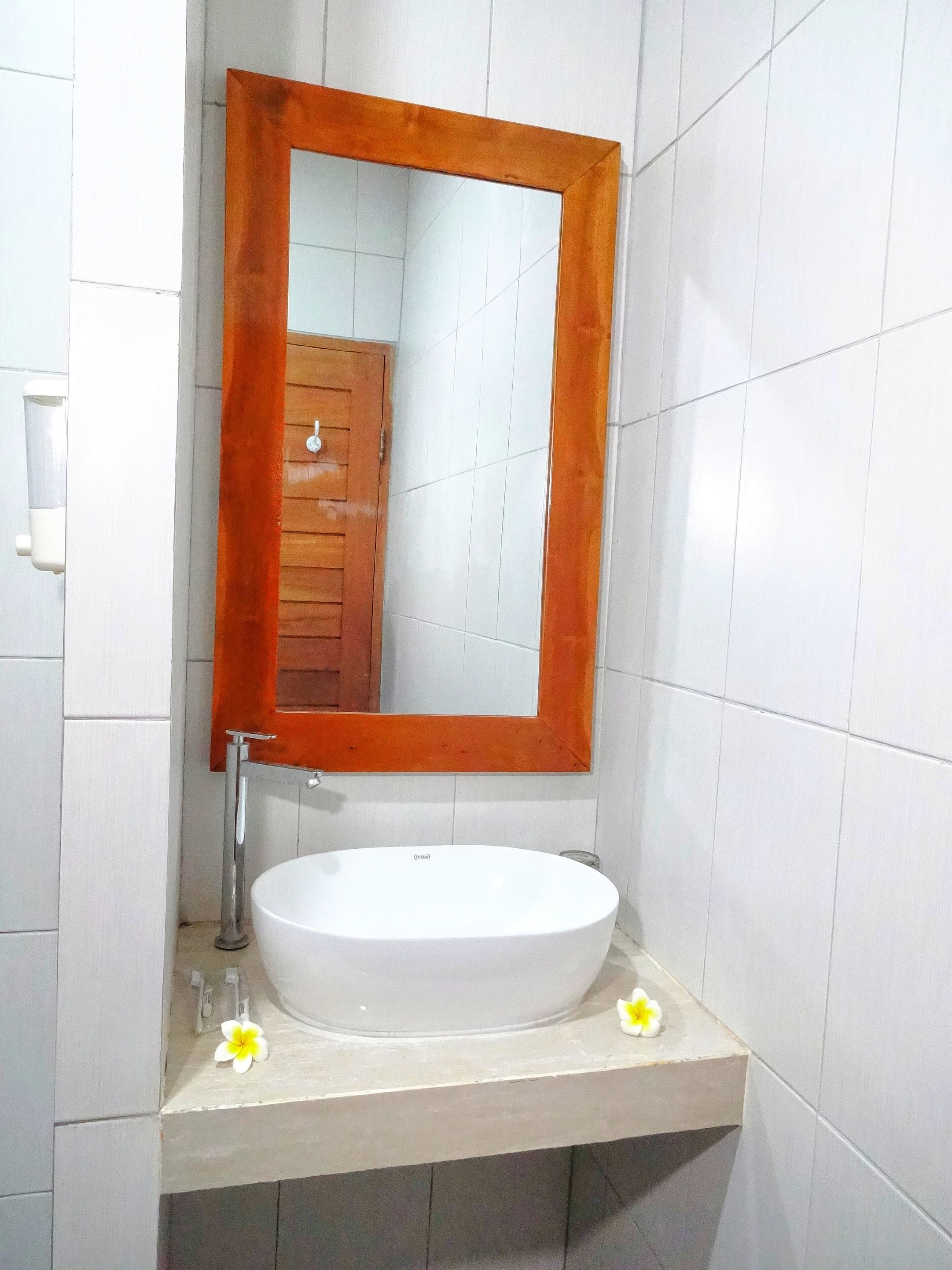 Une salle de bain avec un lavabo blanc, un miroir encadré en bois et des murs recouverts de carreaux blancs.