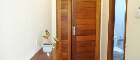 A wooden door with a handle, a small potted plant on a wooden table, and a glimpse of a bathroom with a toilet.