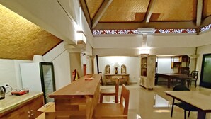 A spacious dining area with a long wooden table and chairs, a kitchen area with cabinets and a stove, and a ceiling with a woven pattern. - Ananda's Sanur (Denpasar)