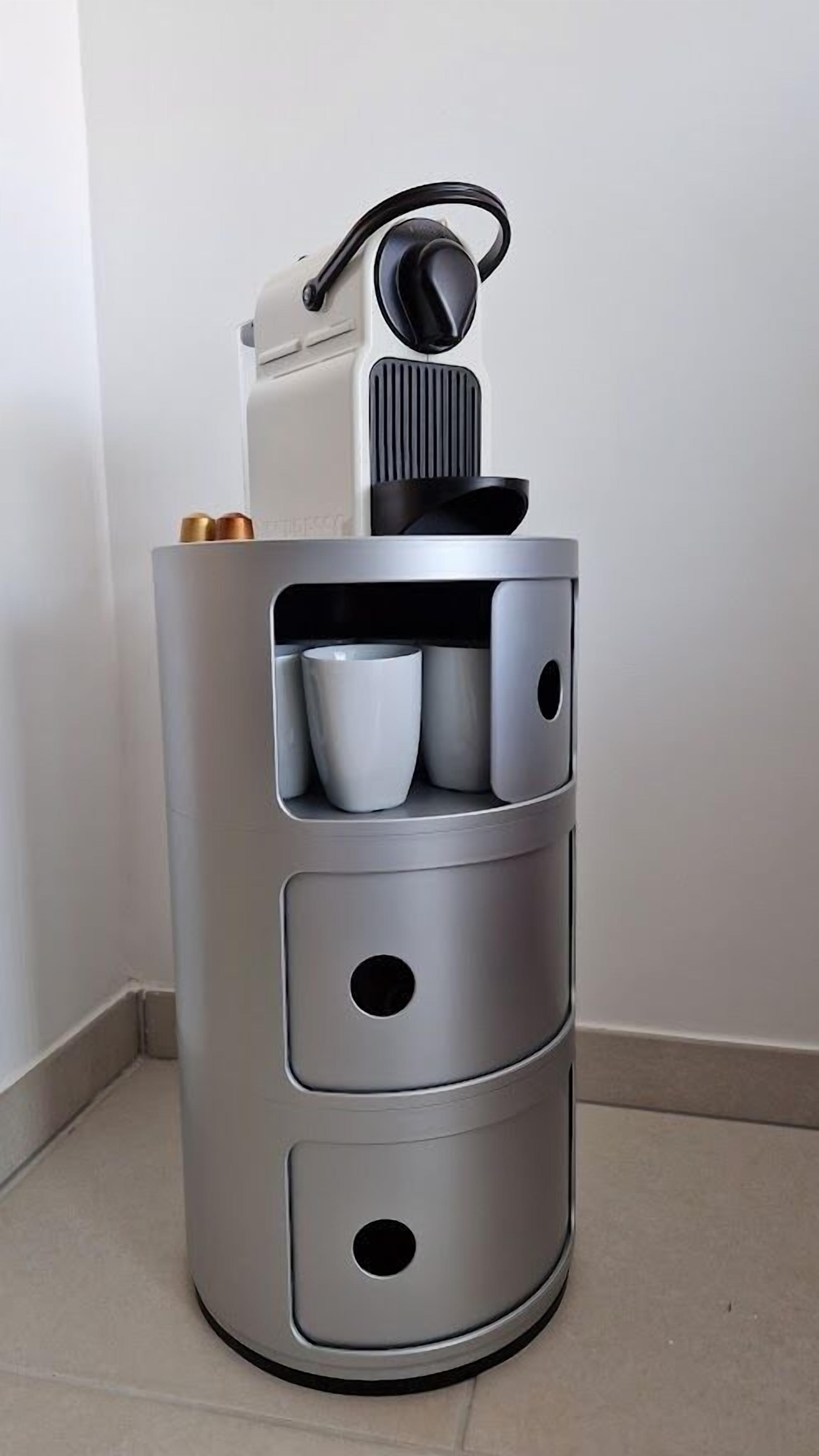 Un mueble cilíndrico con varios compartimentos, que incluye una sección superior con asa y una sección central con tres cajones.